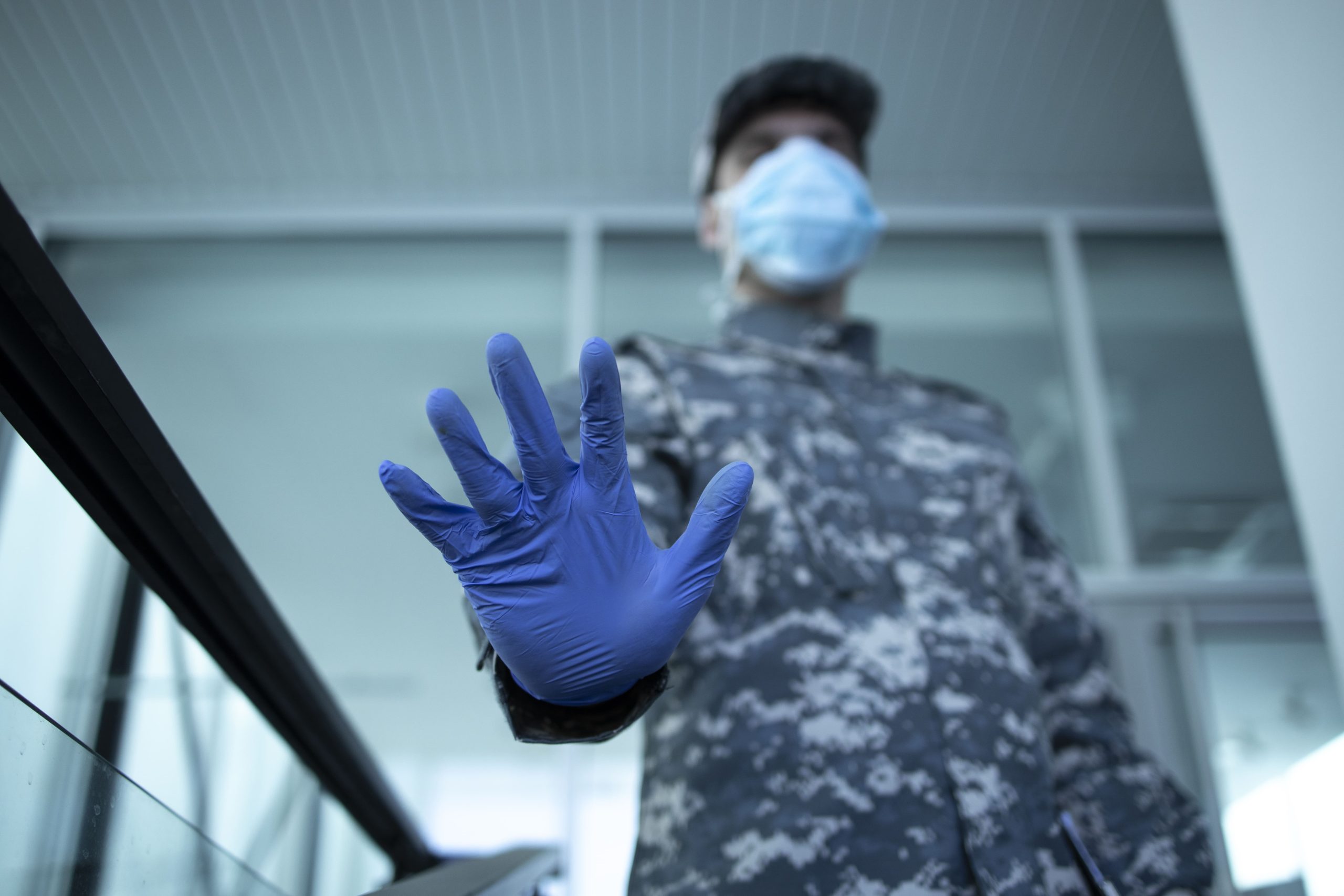 soldier camouflage uniform wearing protective gloves mask showing stop sign hospital entrance 1 scaled